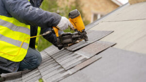 Worker using nail gun to install shingles on roof