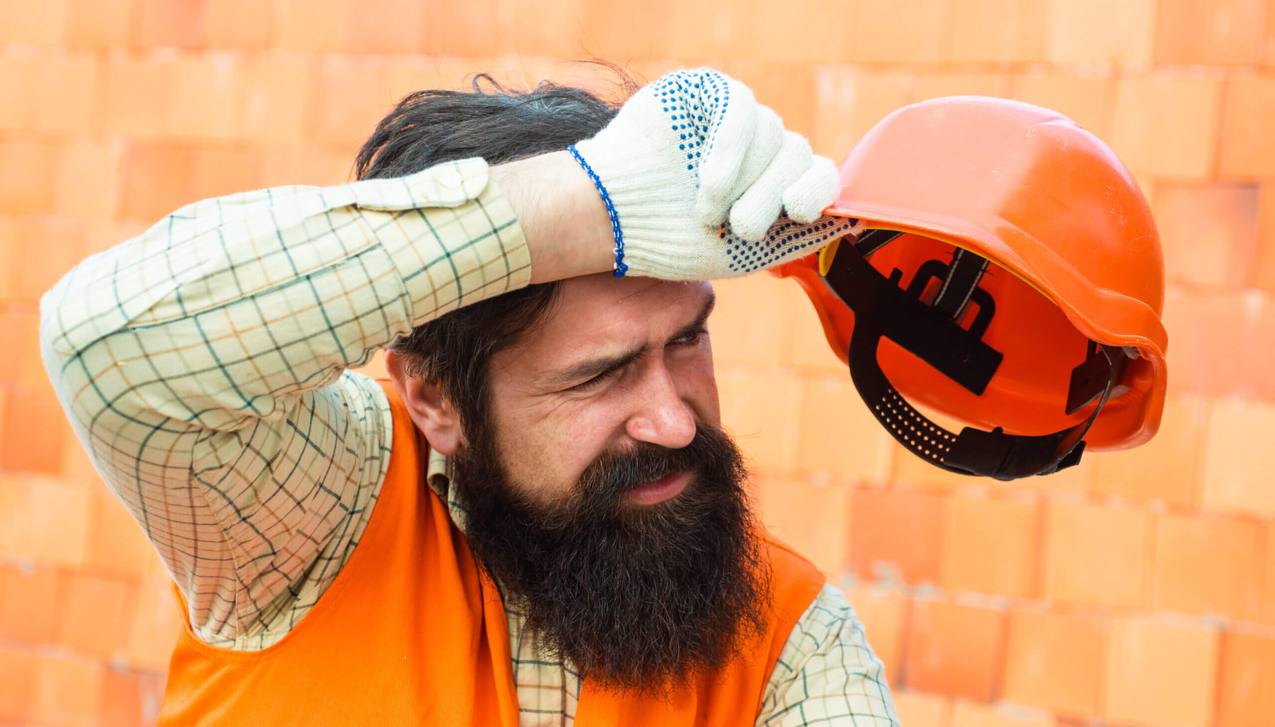 Hard work at a construction site. Heavy profession. Male builder wipes sweat from brow. Tired builder. Physical work in hot weather. Heat and safety at work