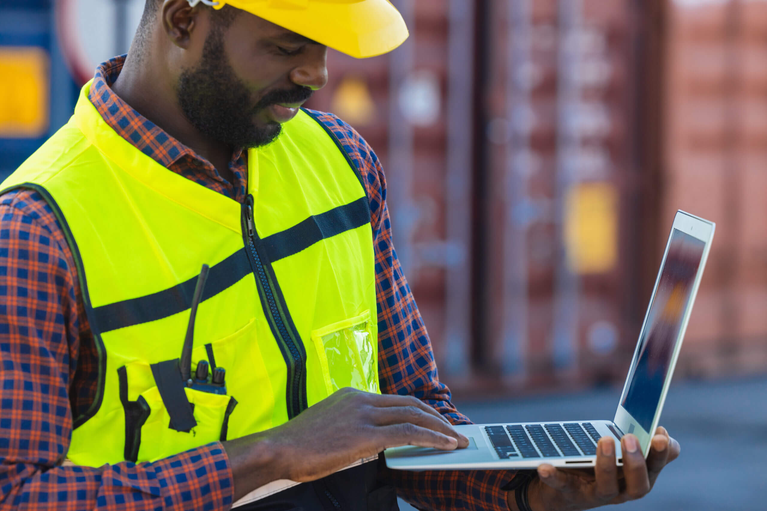 Port cargo staff worker using laptop computer online to manage control loading container in logistics industry.