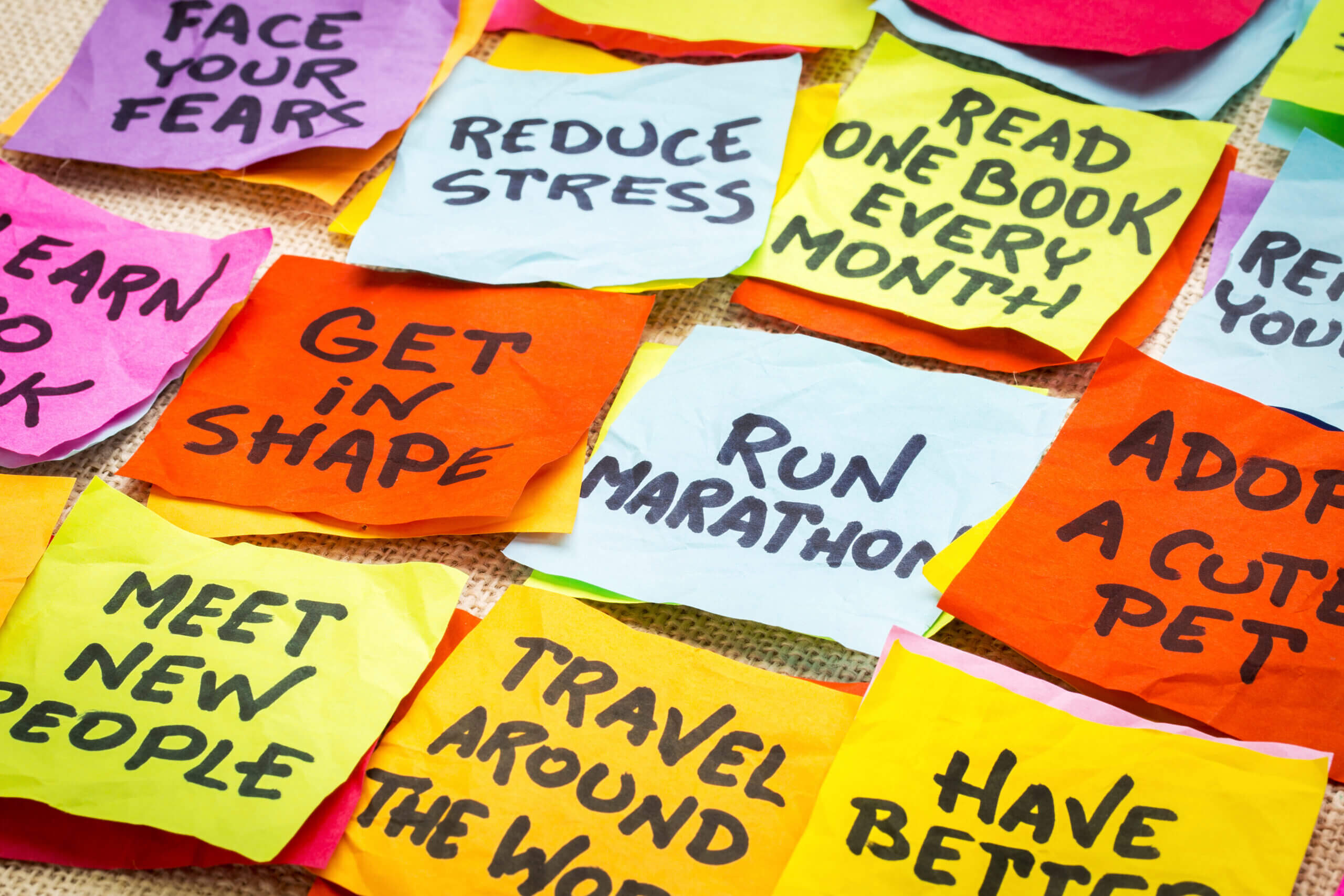 realistic and unrealistic new year goals or resolutions - colorful sticky notes on canvas